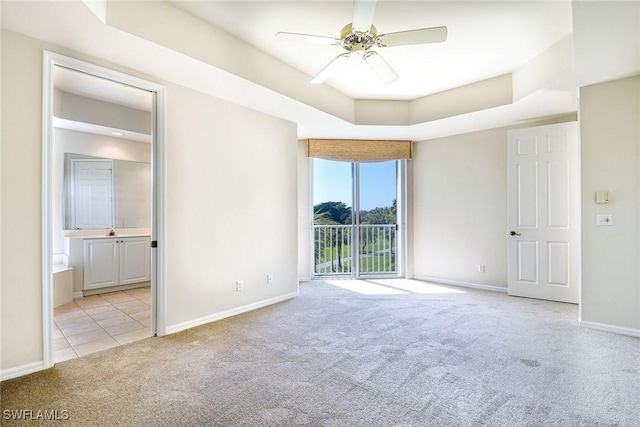 unfurnished bedroom with a tray ceiling, connected bathroom, baseboards, light colored carpet, and access to exterior
