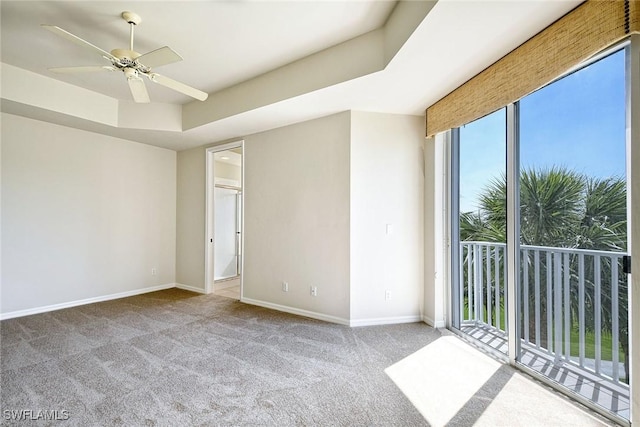carpeted empty room with ceiling fan, a raised ceiling, and baseboards