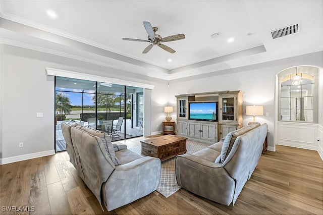 living area with a tray ceiling, wood finished floors, visible vents, and ceiling fan