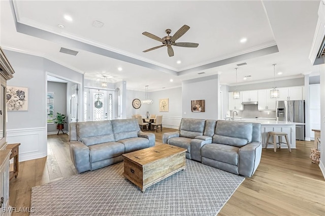 living room with wainscoting, a raised ceiling, and ceiling fan