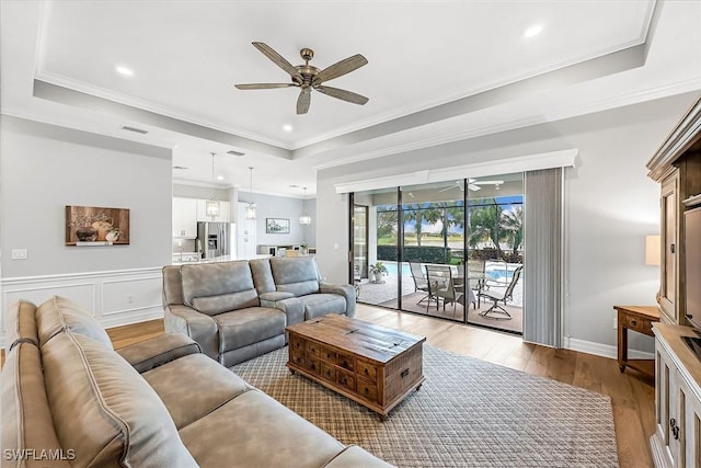 living room featuring visible vents, ceiling fan, light wood-style flooring, and a tray ceiling