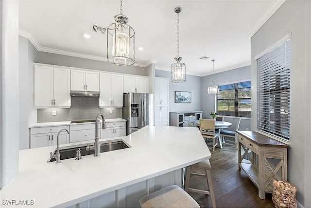 kitchen with a sink, under cabinet range hood, an inviting chandelier, stainless steel fridge with ice dispenser, and decorative backsplash