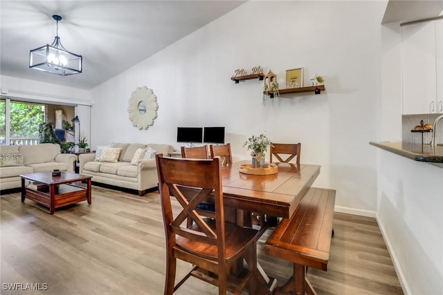 dining area with light wood-type flooring, lofted ceiling, baseboards, and an inviting chandelier