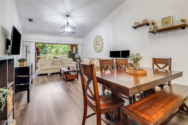 dining area with visible vents, a notable chandelier, vaulted ceiling, and light wood-style flooring