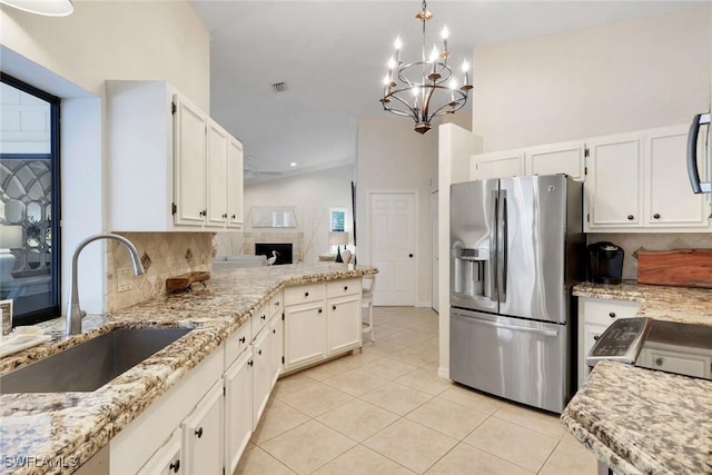 kitchen featuring light stone counters, a sink, stainless steel refrigerator with ice dispenser, backsplash, and light tile patterned flooring