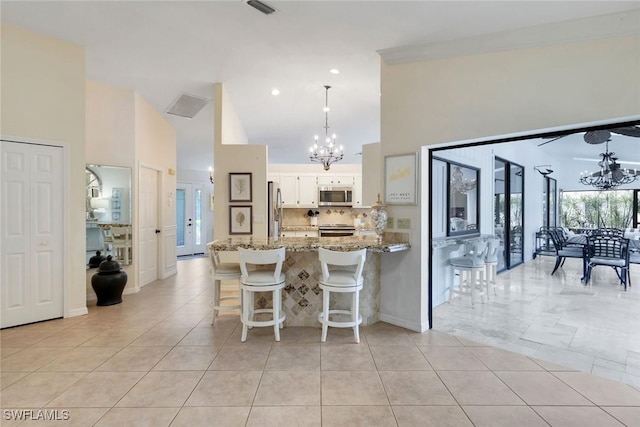 kitchen featuring light stone counters, stainless steel appliances, white cabinetry, a chandelier, and a peninsula