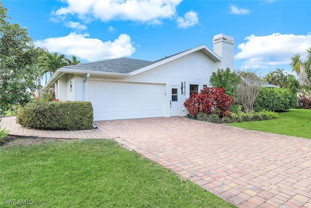 view of side of property with decorative driveway, a chimney, a shingled roof, a lawn, and an attached garage