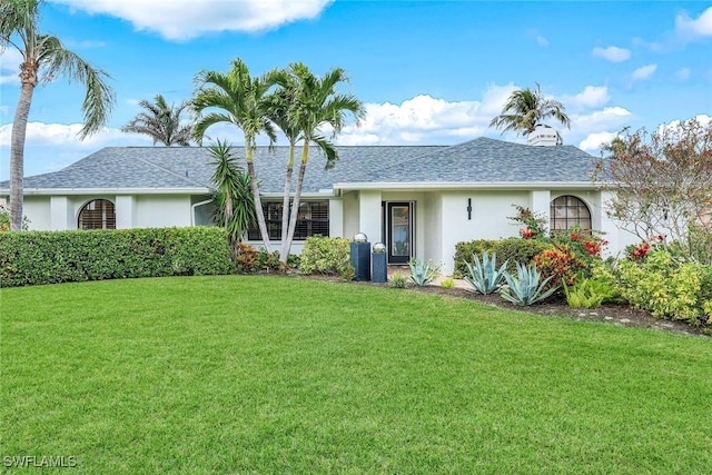 ranch-style home with a front lawn, roof with shingles, and stucco siding