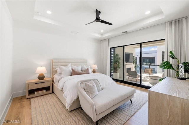 bedroom with light wood finished floors, baseboards, access to outside, a tray ceiling, and recessed lighting