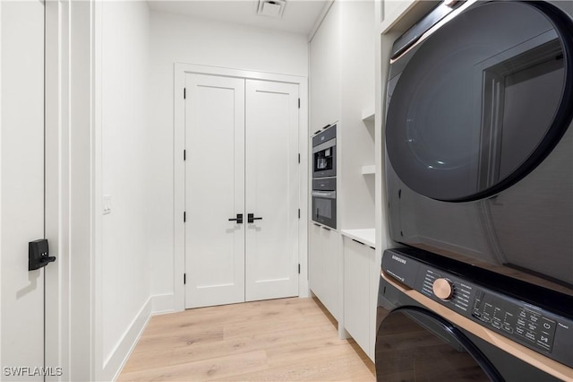 laundry area with visible vents, light wood finished floors, and stacked washer and clothes dryer