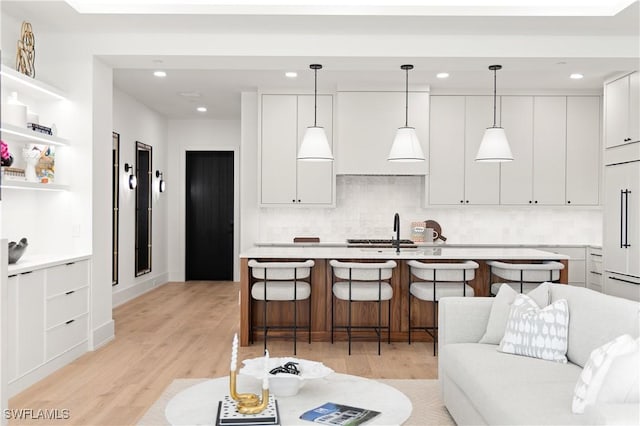 kitchen featuring paneled refrigerator, white cabinets, light countertops, light wood-type flooring, and a kitchen bar