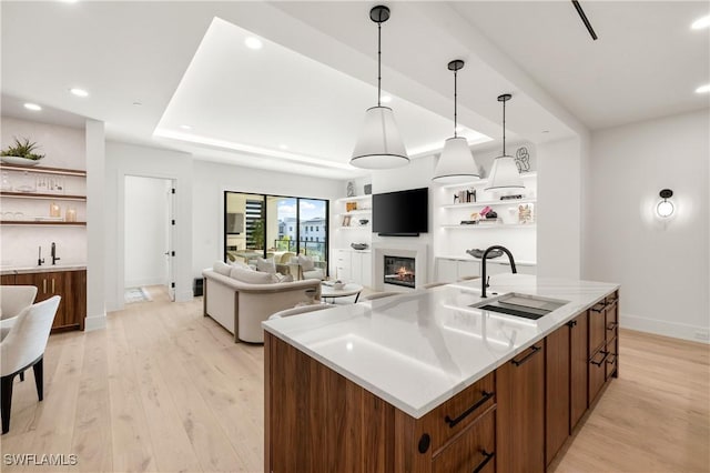 kitchen featuring light wood-style flooring, light countertops, a sink, and a glass covered fireplace