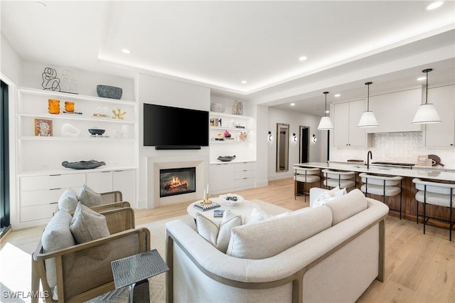 living area with recessed lighting, light wood-style flooring, a tray ceiling, and a glass covered fireplace