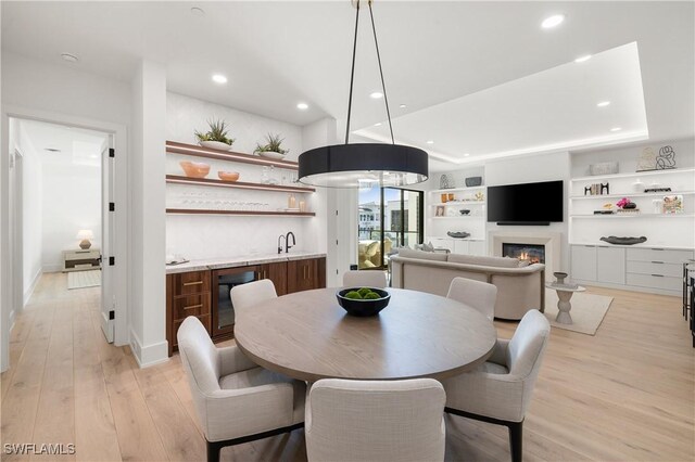 dining area featuring beverage cooler, a glass covered fireplace, light wood-style flooring, wet bar, and recessed lighting