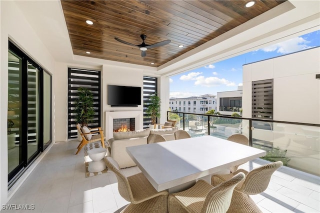 balcony with a warm lit fireplace, ceiling fan, and outdoor dining space