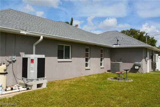 rear view of property with a shingled roof, stucco siding, a yard, and central AC unit