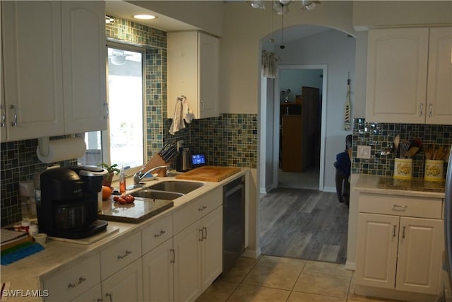 kitchen with arched walkways, light tile patterned floors, light countertops, white cabinetry, and a sink