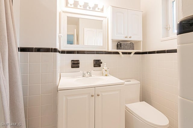 bathroom featuring a wainscoted wall, vanity, toilet, and tile walls