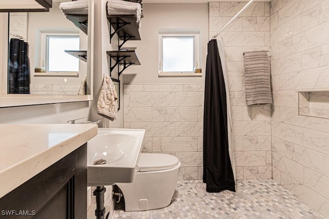 full bath featuring toilet, a wainscoted wall, a tile shower, and tile walls