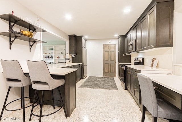 kitchen with stainless steel appliances, a sink, dark brown cabinets, light countertops, and a kitchen bar