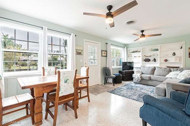 living area featuring light speckled floor, visible vents, and a ceiling fan