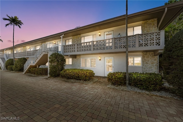 back of property at dusk featuring stone siding, stucco siding, and stairs