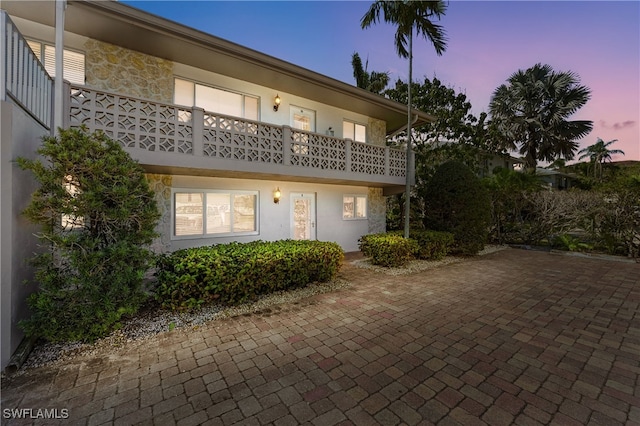 rear view of property with a balcony, stone siding, and stucco siding