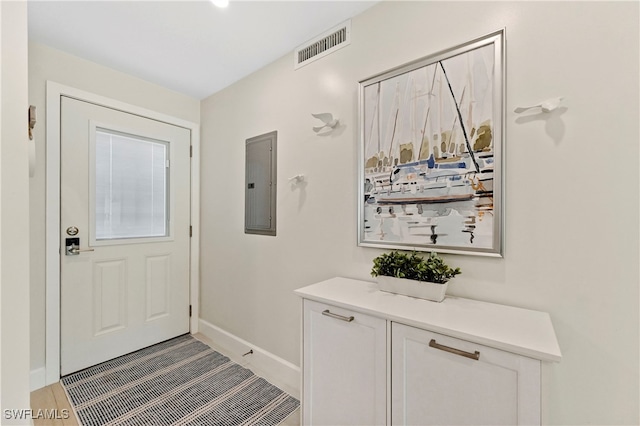 foyer with electric panel, visible vents, and baseboards