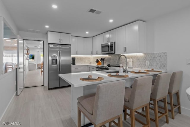 kitchen with visible vents, a peninsula, stainless steel appliances, light countertops, and a sink