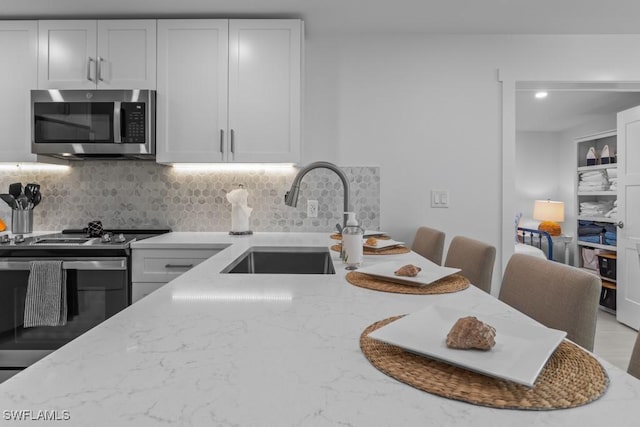 kitchen featuring stainless steel appliances, a sink, backsplash, and light stone countertops