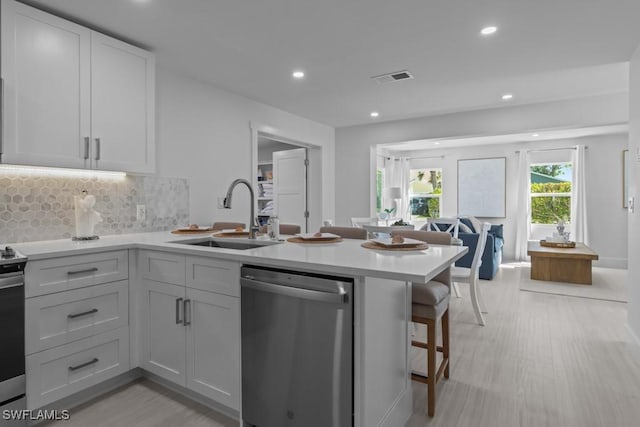 kitchen featuring visible vents, dishwasher, a peninsula, light countertops, and a sink