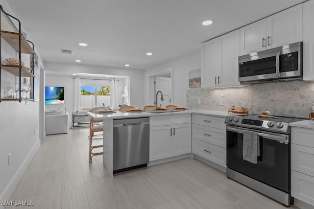 kitchen with decorative backsplash, a peninsula, stainless steel appliances, white cabinetry, and a sink