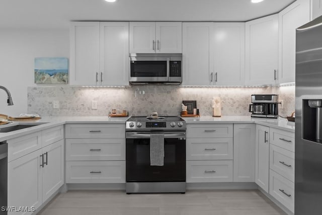 kitchen featuring decorative backsplash, stainless steel appliances, light countertops, white cabinetry, and a sink