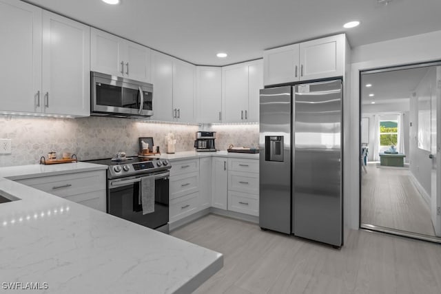 kitchen featuring light wood finished floors, white cabinets, appliances with stainless steel finishes, light stone counters, and backsplash