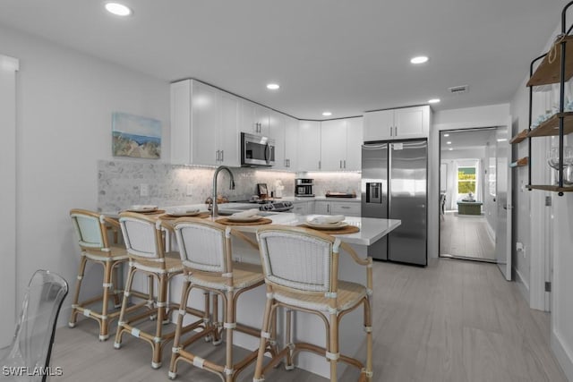 kitchen featuring stainless steel appliances, tasteful backsplash, visible vents, white cabinets, and a peninsula