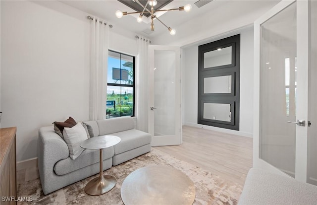 living area featuring french doors, visible vents, wood finished floors, a chandelier, and baseboards