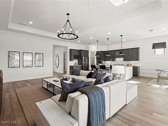 living area with light wood-style flooring, recessed lighting, baseboards, a raised ceiling, and an inviting chandelier