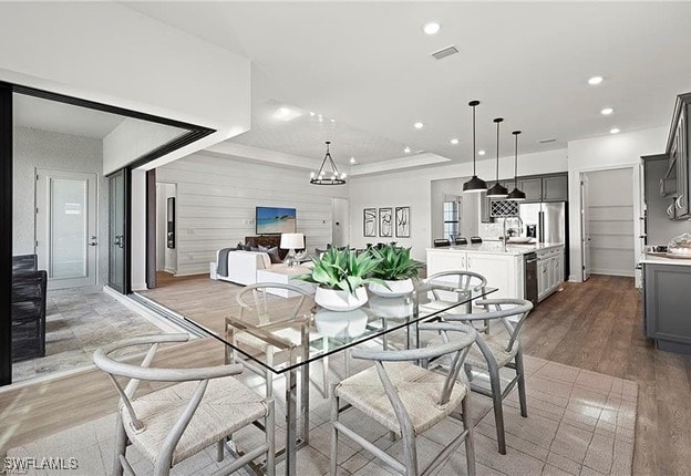 dining room with a tray ceiling, recessed lighting, visible vents, light wood-style flooring, and an inviting chandelier