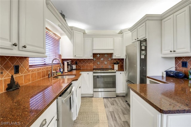 kitchen with tasteful backsplash, appliances with stainless steel finishes, white cabinetry, a sink, and dark stone countertops