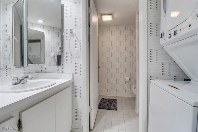 bathroom with tile walls, stacked washer and dryer, toilet, vanity, and tile patterned flooring