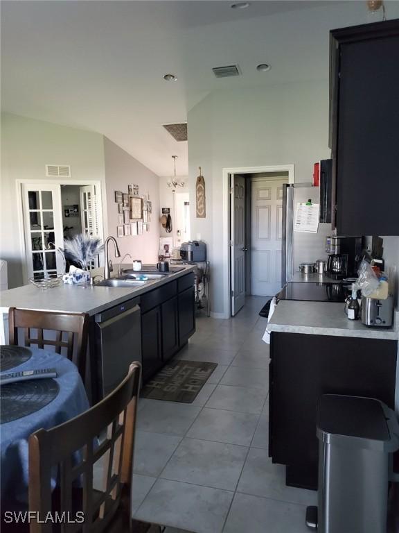 kitchen with light tile patterned floors, visible vents, vaulted ceiling, dark cabinetry, and a sink