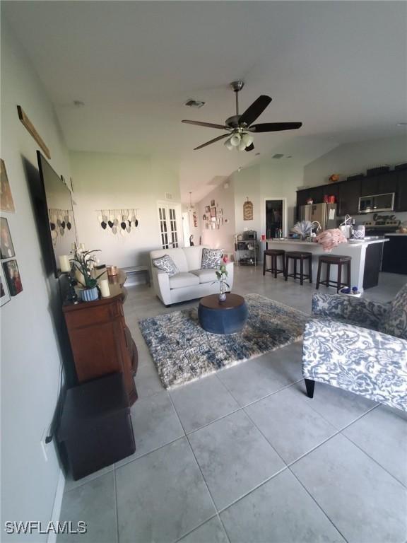 living room featuring vaulted ceiling, visible vents, tile patterned flooring, and a ceiling fan