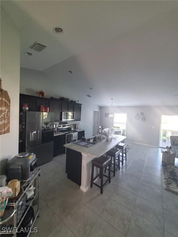 kitchen featuring light tile patterned floors, a kitchen island, visible vents, a kitchen breakfast bar, and appliances with stainless steel finishes