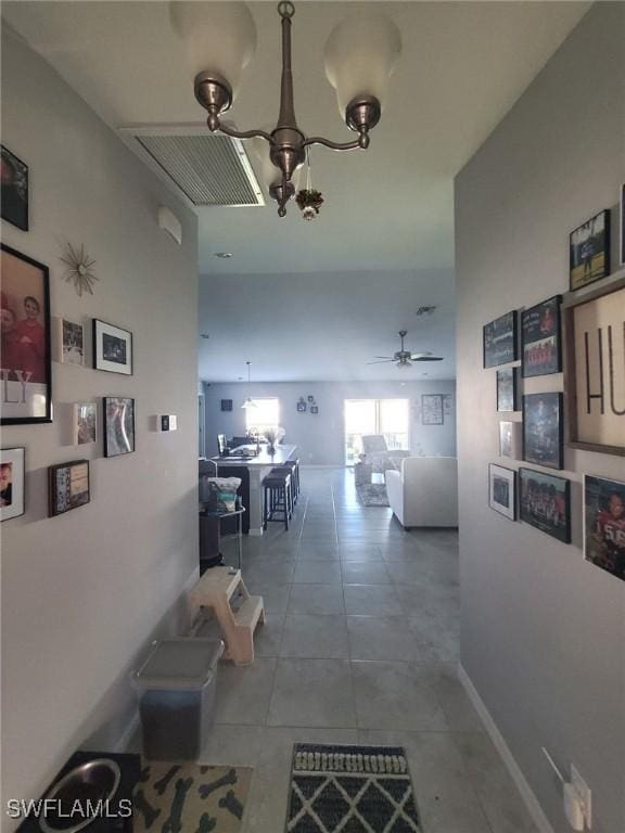 hallway featuring tile patterned flooring, baseboards, and an inviting chandelier