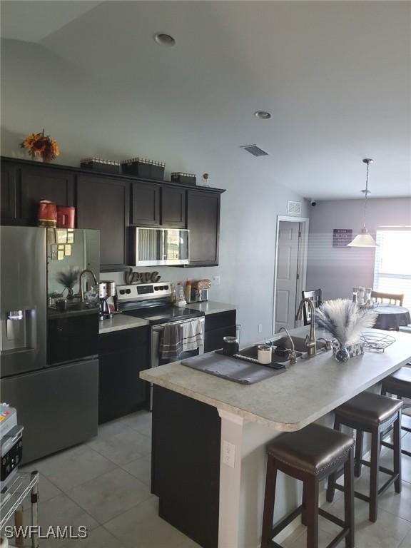 kitchen with light tile patterned floors, visible vents, a breakfast bar, stainless steel appliances, and light countertops