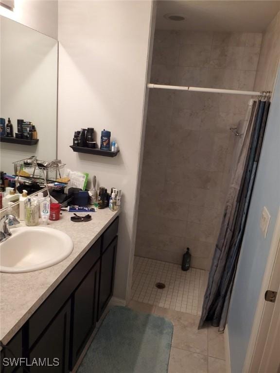 bathroom featuring tile patterned flooring, a tile shower, and vanity