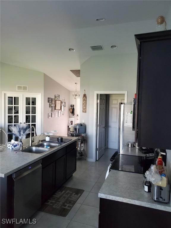 kitchen featuring light tile patterned floors, a sink, vaulted ceiling, freestanding refrigerator, and dishwasher