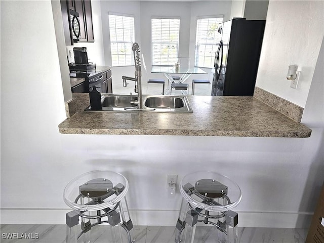 kitchen featuring black appliances, a breakfast bar area, a peninsula, and a sink