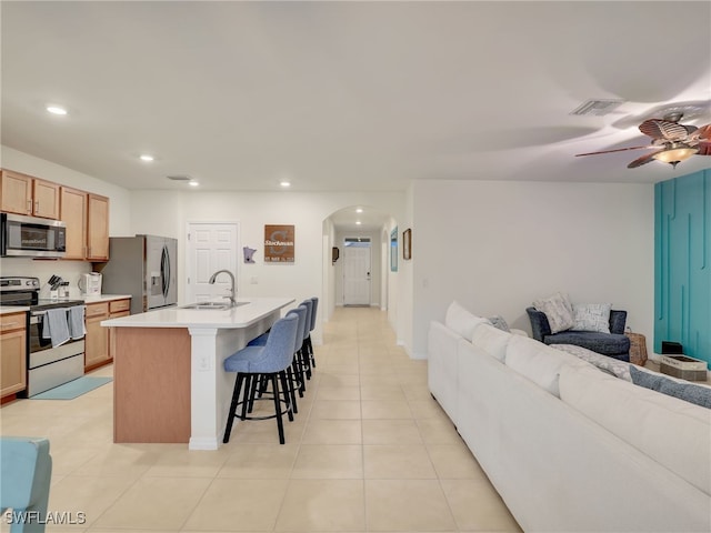 kitchen with arched walkways, open floor plan, stainless steel appliances, a kitchen bar, and a sink