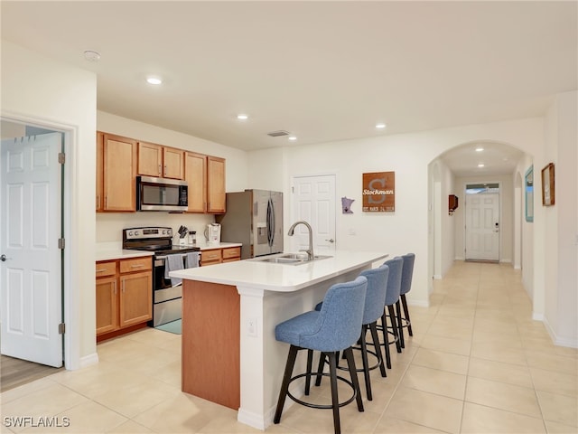 kitchen featuring arched walkways, a sink, a kitchen breakfast bar, appliances with stainless steel finishes, and a center island with sink